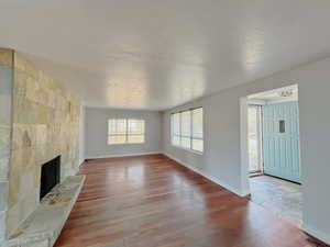 Unfurnished living room with a tiled fireplace, wood finished floors, and a textured ceiling