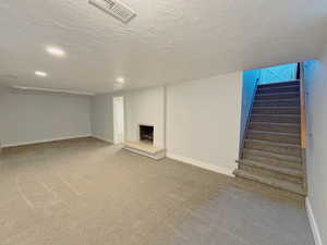 Finished below grade area featuring a fireplace with raised hearth, stairs, recessed lighting, carpet floors, and a textured ceiling