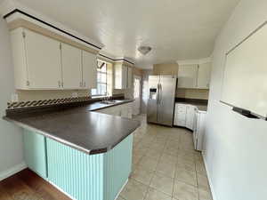 Kitchen with stainless steel fridge, dark countertops, a peninsula, and white cabinetry
