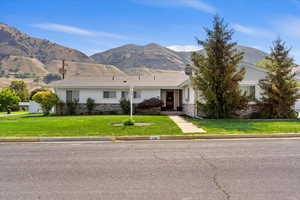 Ranch-style home with a mountain view, a front yard, and stone siding