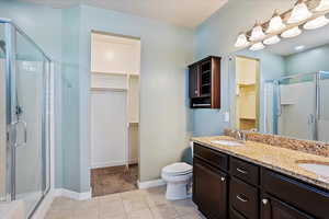 Full bath with a spacious closet, a stall shower, double vanity, and tile patterned flooring