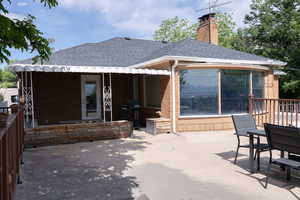 Back of house featuring roof with shingles, brick siding, a patio, and a chimney