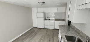 Kitchen with white appliances, decorative backsplash, wood finished floors, a textured ceiling, and white cabinetry