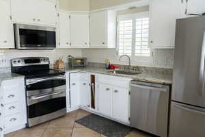 Kitchen featuring appliances with stainless steel finishes, decorative backsplash, light tile patterned floors, white cabinetry, and light stone counters