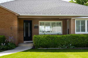 View of exterior entry featuring a shingled roof, brick siding, and a yard