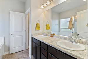 Bathroom featuring a bath, double vanity, stone finish floors, and recessed lighting
