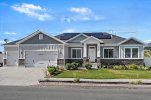 Craftsman house with stone siding, an attached garage, and roof mounted solar panels
