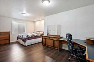 Bedroom featuring a textured ceiling, an office area, and dark wood-style flooring