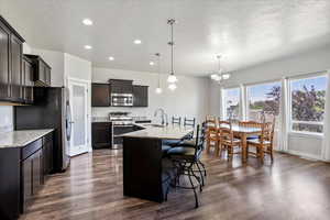 Kitchen with stainless steel appliances, recessed lighting, a chandelier, dark wood-style flooring, and a center island with sink