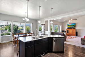Kitchen with stainless steel dishwasher, open floor plan, dark cabinets, light stone countertops, and vaulted ceiling
