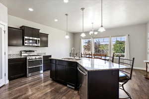 Kitchen featuring appliances with stainless steel finishes, a breakfast bar, a chandelier, dark wood finished floors, and recessed lighting