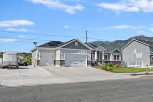 View of front of house with board and batten siding, a garage, a mountain view, roof mounted solar panels, and stone siding