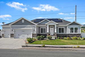 Craftsman-style house with board and batten siding, a front lawn, stone siding, a garage, and driveway