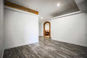 Empty room with arched walkways, dark wood-type flooring, and recessed lighting