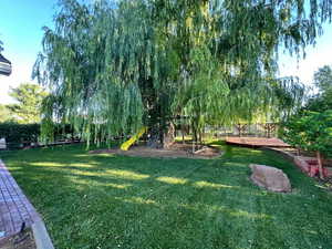 View of green lawn featuring a playground and a wooden deck