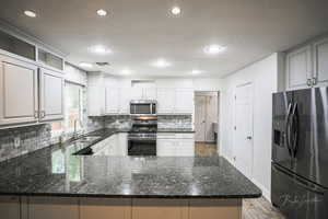 Kitchen with appliances with stainless steel finishes, decorative backsplash, a peninsula, a textured ceiling, and dark stone countertops
