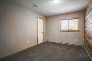 Carpeted empty room with a textured ceiling and baseboards