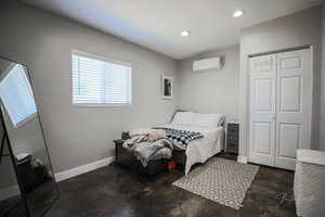 Bedroom with a wall mounted AC, unfinished concrete flooring, a closet, and recessed lighting