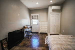Bedroom featuring a wall unit AC, finished concrete flooring, recessed lighting, and a textured wall