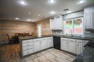 Kitchen featuring black dishwasher, a peninsula, a textured ceiling, tasteful backsplash, and white cabinets