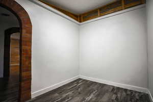 Empty room with arched walkways and dark wood-style floors