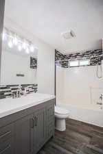 Full bath with wood finished floors, vanity, shower / bath combination, decorative backsplash, and a textured ceiling
