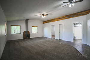 Unfurnished living room featuring ceiling fan, a wood stove, vaulted ceiling, and dark wood-style floors