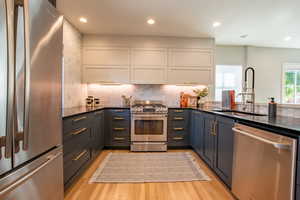 Kitchen with stainless steel appliances, white cabinetry, light wood-style flooring, decorative backsplash, and recessed lighting