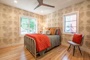 Main level bedroom with multiple windows, light wood finished floors, recessed lighting, and ceiling fan