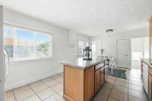 Kitchen with light tile patterned flooring, white appliances, a center island, and brown cabinets
