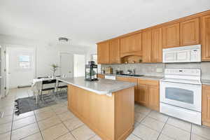 Kitchen featuring white appliances, light tile patterned flooring, tasteful backsplash, a kitchen island, and light countertops
