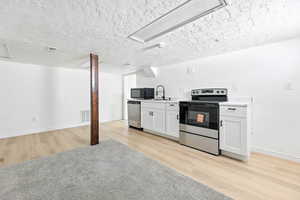 Kitchen with stainless steel appliances, light wood-style floors, a textured ceiling, light countertops, and white cabinetry