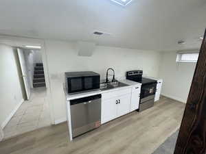 Kitchen featuring appliances with stainless steel finishes, light wood-type flooring, white cabinetry, and light countertops