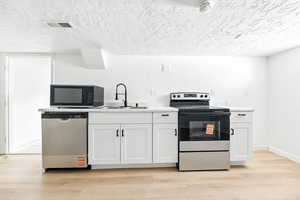 Kitchen featuring a textured ceiling, stainless steel appliances, white cabinets, light countertops, and light wood-type flooring