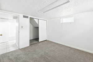 Unfurnished bedroom with carpet floors, a textured ceiling, a closet, and tile patterned flooring