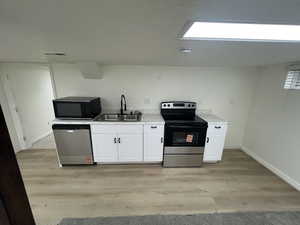 Kitchen featuring appliances with stainless steel finishes, light wood-style floors, white cabinets, and light countertops