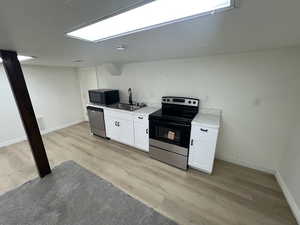 Kitchen with stainless steel appliances, white cabinetry, light wood-style floors, and light stone countertops