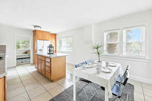 Kitchen with light tile patterned floors, white fridge with ice dispenser, a center island, and light countertops