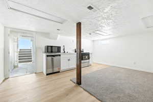 Kitchen featuring a textured ceiling, white cabinets, light wood-type flooring, stainless steel appliances, and light countertops