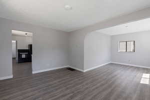 Unfurnished room featuring dark wood-style floors, arched walkways, and a textured ceiling