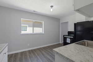 Kitchen featuring black appliances, dark wood-type flooring, a textured ceiling, white cabinetry, and light countertops