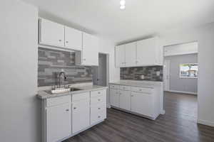 Kitchen featuring decorative backsplash, light countertops, a textured ceiling, white cabinets, and dark wood-style flooring