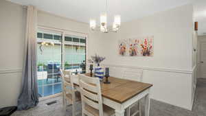 Carpeted dining area with a chandelier and patio access