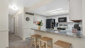 Kitchen with black appliances, a peninsula, light colored carpet, backsplash, and a breakfast bar area
