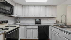 Kitchen featuring black appliances, white cabinetry, decorative backsplash, and light countertops