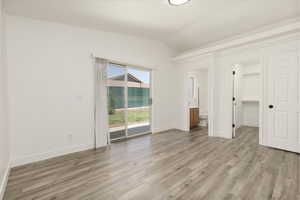 Unfurnished bedroom featuring access to exterior, lofted ceiling, light wood-style flooring, ensuite bathroom, and a walk in closet