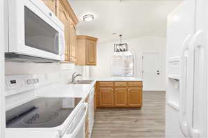 Kitchen with white appliances, light wood-type flooring, a chandelier, vaulted ceiling, and light countertops