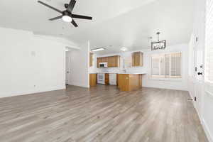 Unfurnished living room featuring a chandelier, lofted ceiling, light wood finished floors, and a ceiling fan