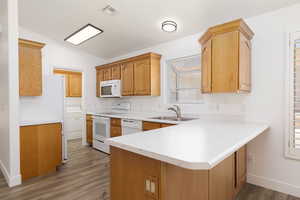 Kitchen featuring white appliances, a peninsula, light wood-type flooring, washer / clothes dryer, and vaulted ceiling