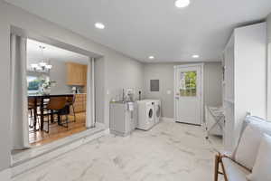 Laundry area featuring washing machine and clothes dryer, electric panel, recessed lighting, a chandelier, and light marble finish floors